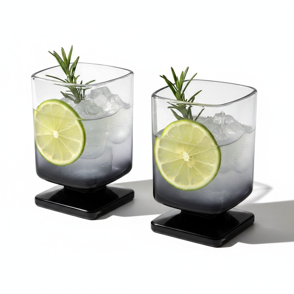 Dois copos de vidro quadrados Cucinamup com degradê preto, contendo gelo, rodela de limão e alecrim para drinks.