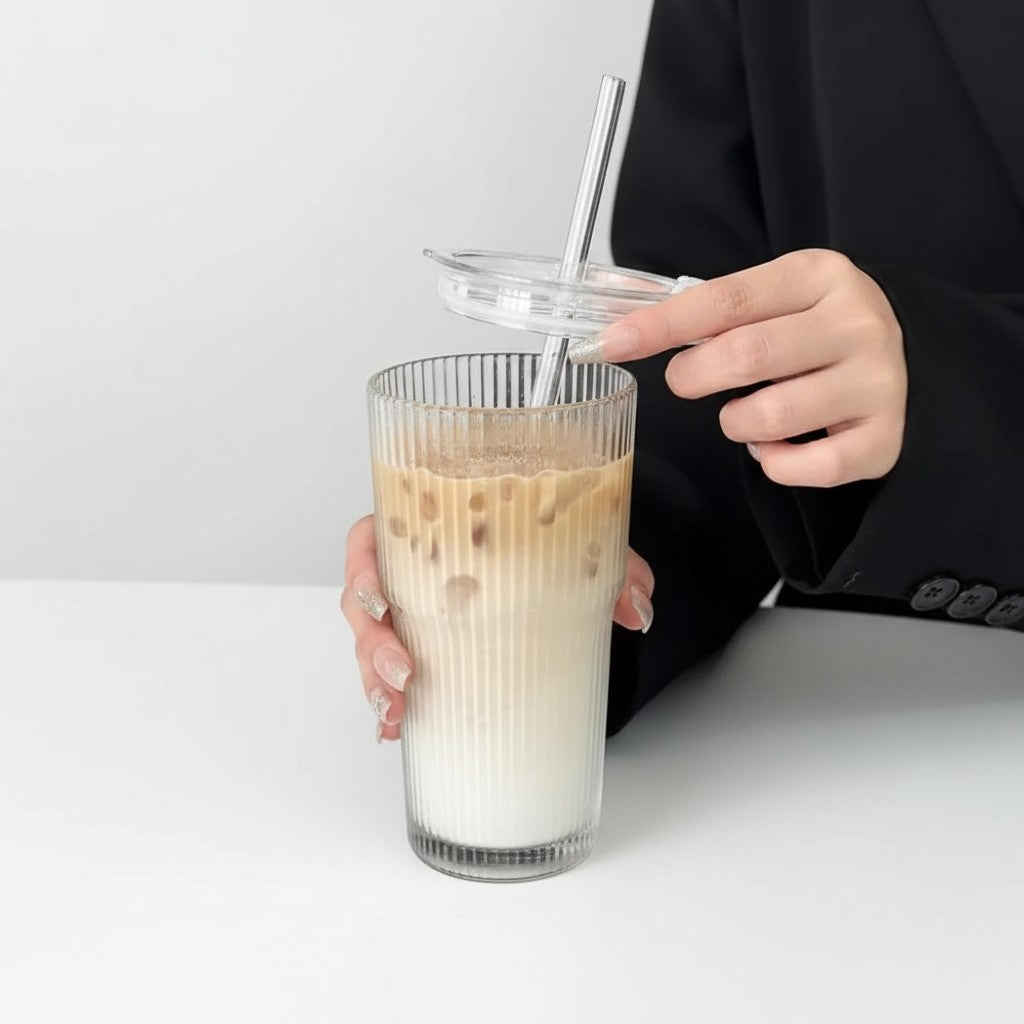 Copo de vidro canelado Cucinamup de 600ml com tampa e canudo metálico, contendo café gelado com leite.