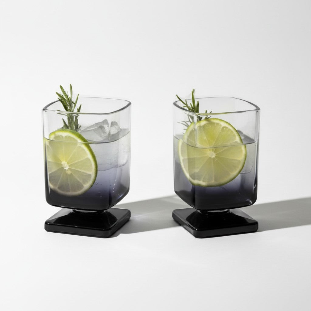 Dois copos de vidro quadrados Cucinamup com degradê preto, contendo drinks com gelo, limão e alecrim.