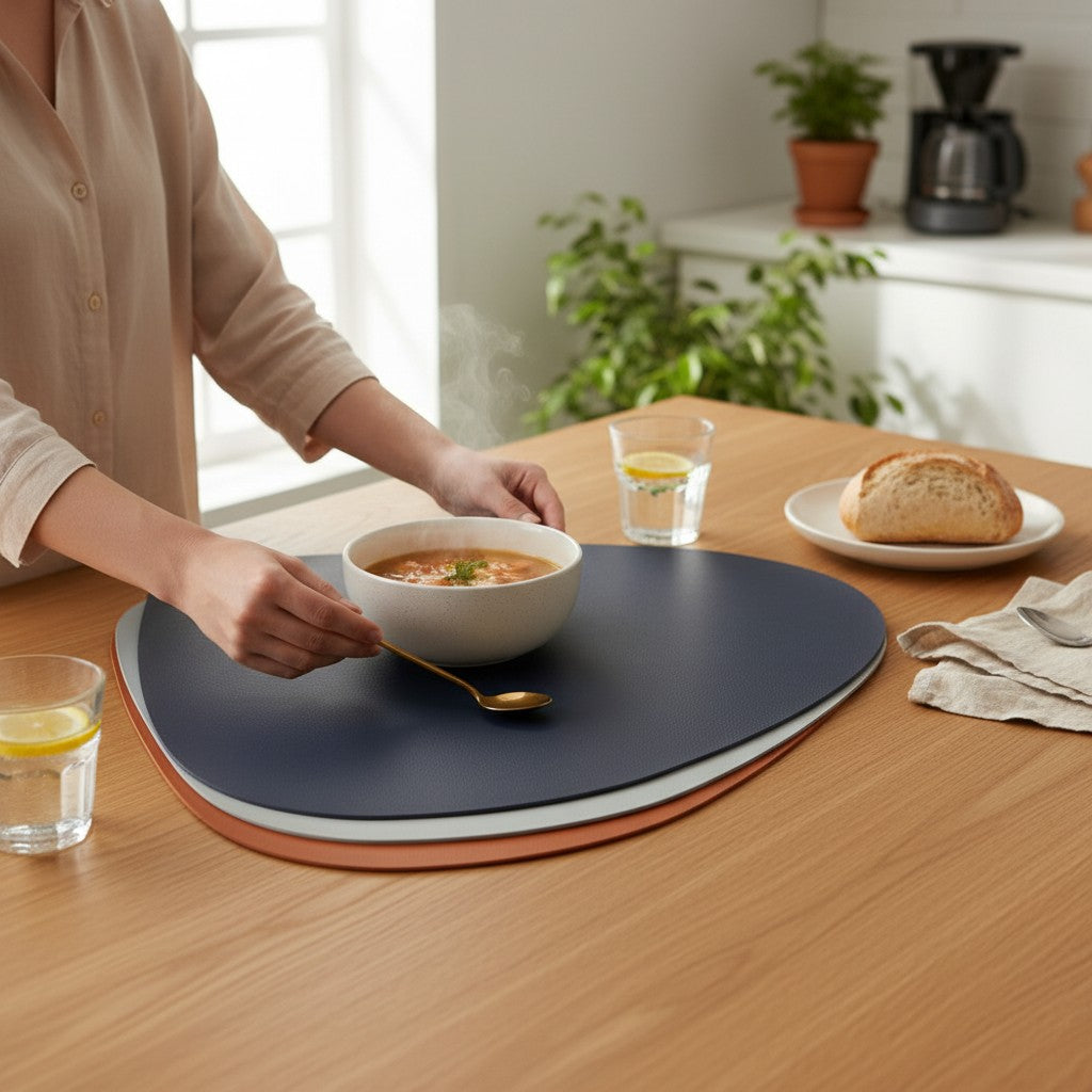 Jogo americano Cucinamup em formato de gota, feito de couro sintético premium, sobre mesa de madeira com prato de sopa.