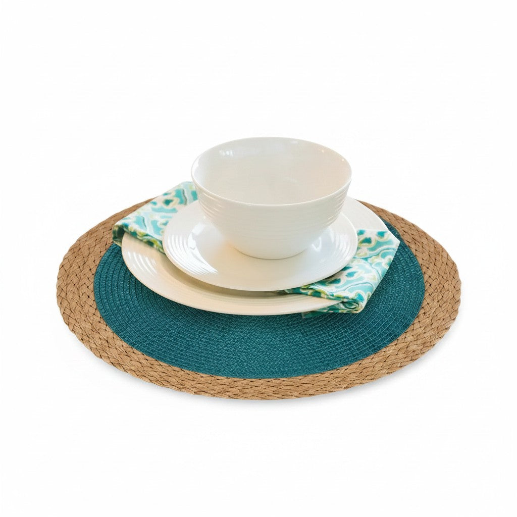 Jogo americano redondo trançado Cucinamup azul pavão com borda bege, decorado com pratos brancos e guardanapo estampado