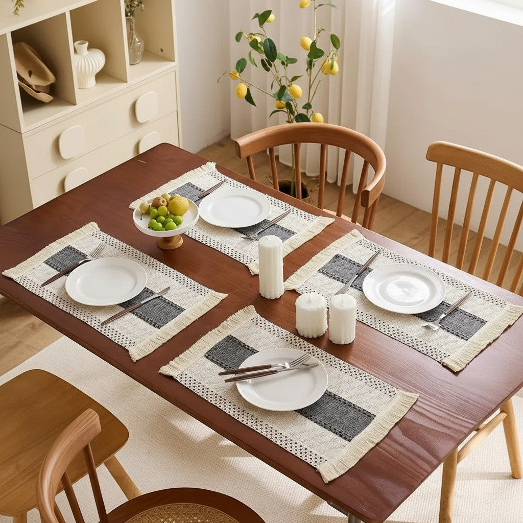 Jogo americano retangular Cucinamup com tecido tramado, listras e franjas em mesa de madeira posta para quatro pessoas.