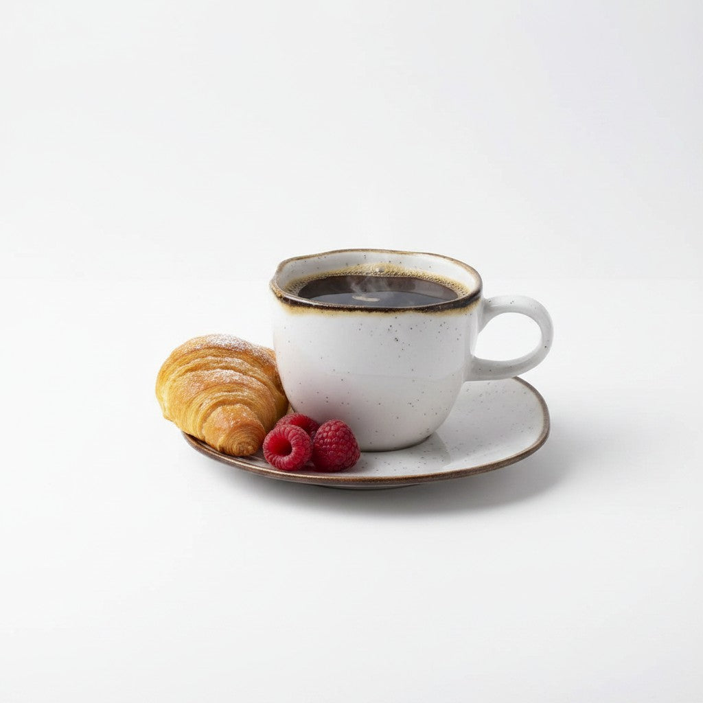 Xícara e pires Cucinamup da linha Oxford Maresia em porcelana branca com detalhes marrons, servindo café e croissant.
